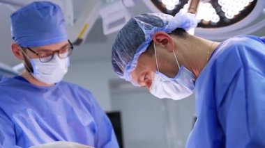 Erkek cerrah ve asistanı beyin cerrahisi yapıyor. Operasyonda çalışan doktorun yan görünüm portresi.