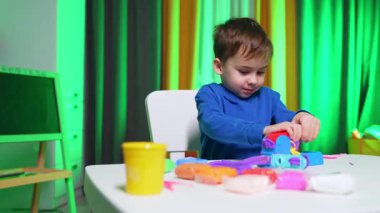 Mavi kazaklı sevimli erkek bebek pervaz makinesine baskı yapıyor. Çocuk cihazdan plastik karıştırıcı alıyor..
