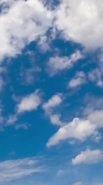 Güzel küçük beyaz bulutlar gökyüzünde uçar ve rüzgarda dağılır. Düşük açı. Zaman ayarlı. Dikey video