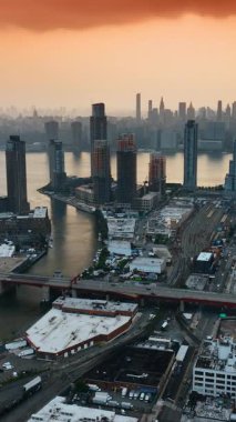 Günbatımında New York 'un görkemli manzarasının üzerinde turuncu gökyüzü. Nakliye gemisi Metropolis 'in yol sisteminden geçiyor. Hava görüntüsü. Dikey video