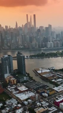 Gün batımında New York 'un puslu manzarası. Turuncu gökyüzünün altında çarpıcı gökdelenler. Queensboro Köprüsü 'nü tepeden izleyin. Dikey video