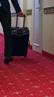 Otel koridorunda bagajı olan tanınmamış bir iş adamı. Elinde bavul olan bir adam otel koridorunda yürüyor. Dikey video