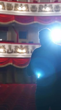 Tiyatroda bir spiker. Bir kişinin parlak yuvarlak ışığı. Siyah takım elbiseli adam konser salonuna gidiyor. Arkadan bak. Dikey video