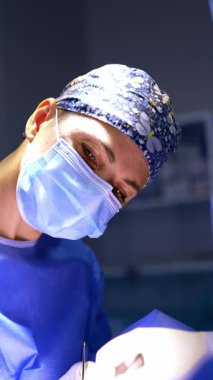 Maskeli ve şapkalı kadın cerrahın kendinden emin yüzü. Doktorun portresi alet ve aletlerle yapılmış. Dikey video.