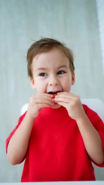 Beyaz, tatlı bir çocuk ağzına bir parça portakal koyar. Mutlu bebek meyve yiyor. Düşük açı. Dikey video.