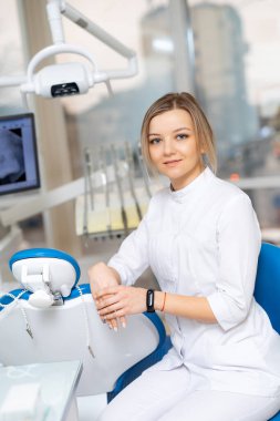 Yeni klinikte genç bir dişçi. Bir diş hekimi, modern ekipmanlarla tedavi için hazır, parlak bir klinikte güven içinde oturur..