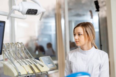 Diş asistanı hasta için hazır. Beyaz önlüklü bir dişçi asistanı, klinikte yapılacak olan hasta randevusuna hazırdır..