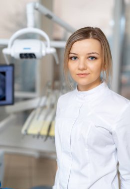 Modern klinikteki dişçi. Genç bir diş hekimi, parlak bir klinikte özen ve uzmanlık sahibi hastalara yardım etmeye hazır bir şekilde poz verir..