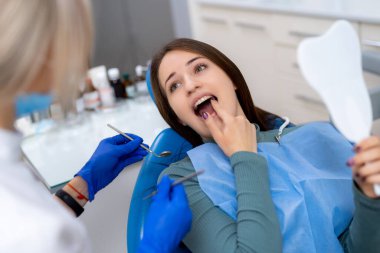 Mutlu bir hastaya diş muayenesi. Modern bir klinikte diş tedavisi gören genç bir kadın, randevusu sırasında dişçiyle meşgul olurken gülümsüyor..