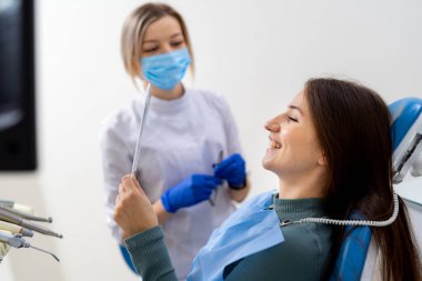 Dişçide gülümseyen kadın. Bir dişçi modern bir diş muayenehanesinde kontrol için gerekli aletleri hazırlarken hasta gülümsüyor ve dostane bir ortam yaratıyor..