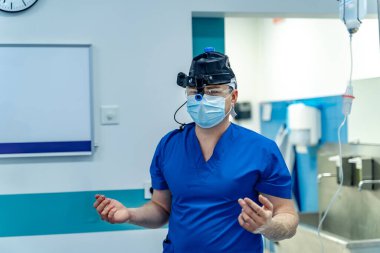 Cerrah ameliyata hazır. Mavi önlüklü ve maskeli bir cerrah modern bir ameliyathanede hazır bekliyor..