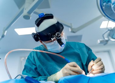 Cerrahlar karmaşık ameliyatlar yaparlar. Bir cerrah, iyi donanımlı bir ameliyathanede far takarken hassas bir ameliyata odaklanır..