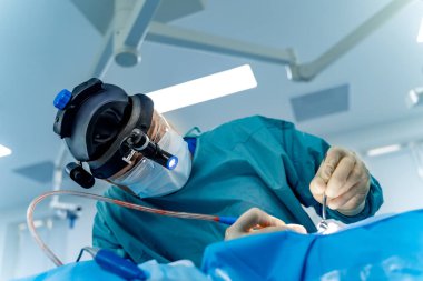 Cerrah hassas bir ameliyat yapıyor. Yetenekli bir cerrah modern bir ameliyathanede karmaşık bir işlem için gelişmiş aletler ve ışıklandırma kullanır..