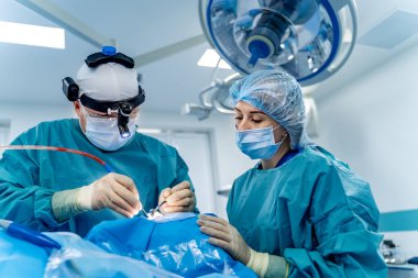 Cerrahlar hassas ameliyatlar yaparlar. İki cerrah, ameliyat sırasında parlak ışıklar altında görevlerine odaklanarak birlikte çalışırlar..