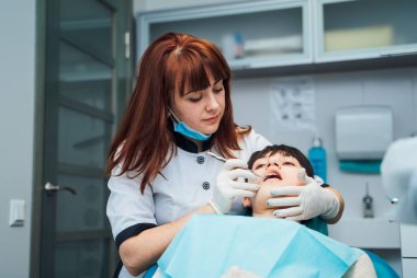 Klinikte diş tedavisi gören bir çocuk. Bir diş hekimi, klinik ortamdaki bir randevu sırasında çocuğun dişlerini muayene eder ve.