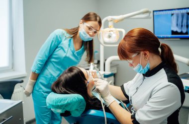 Dişçi klinikteki hastayı tedavi ediyor. Modern bir klinik ortamında iki diş hekimi hastaya oral tedavide yardımcı olur..