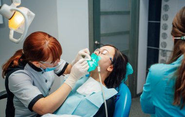 Modern diş muayenesi. Çağdaş bir diş sağlığı kliniğinde mavi bir sandalyede oturan bir hasta diş bakımı alır..