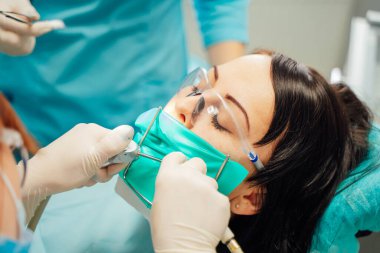 Modern klinikte diş bakımı. Bir hasta, iyi aydınlatılmış bir klinik ortamında odaklanmış bir diş hijyenisti ile diş tedavisi geçirir..