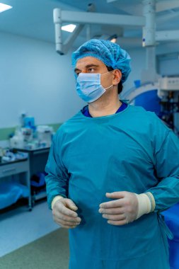 Cerrah ameliyathanede hazırlanıyor. Ameliyat odasında ameliyat maskesini takmış bir cerrah tıbbi müdahale için hazır bekliyor..