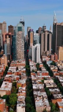 Gökdelenlerin arka planında birkaç katlı evler olan yeşil alan. Güneşli bir günde İHA görüntülerinden New York şehri manzarası. Dikey video