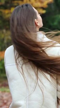 Parkta yürüyen hoş bir kadının portresi. Genç ve güzel bir kadın sonbahar ormanında yürüyor. Dikey video