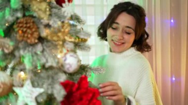 Mutlu kadın süsleme ağacı. Kıvırcık saçlı bir kadın mutlu bir şekilde Noel ağacını süs ve ışıklarla süslüyor..