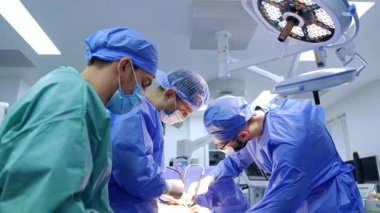 Hastanede çalışan cerrahlar var. Cerrahi önlüklü üç tıp uzmanı modern bir ameliyathanede bir prosedüre odaklanmış durumda..