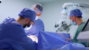 Cerrahlar kısırken ameliyat ederler. Ameliyat önlüğü ve maskeli bir cerrah ekibi temiz ve iyi donanımlı bir ameliyathanede cerrahi bir operasyon gerçekleştiriyor..
