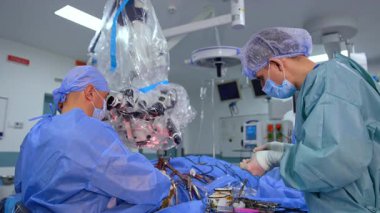 Cerrahlar ameliyathanede. Önlüklü iki maskeli cerrah gelişmiş ekipman, ekip çalışması ve hassasiyetle ameliyat yapıyorlar..