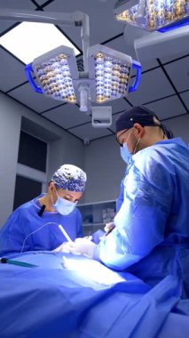 Bir erkek doktorun yardımıyla cerrah ameliyat yapar. Kadın doktor ameliyatta elektrikli aletler kullanır. Düşük açı. Dikey video.
