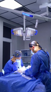 İki beyaz cerrah ameliyathanede lambanın altında çalışıyor. Profesyonel doktor elektrikli alet uyguluyor. Dikey video.