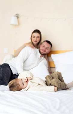 Sıcak yatakta aile bağları kurma zamanı. Rahatlamış bir aile, bir yatakta, bir çocukla oyun oynarken, ebeveynler sevgi dolu bir kucaklaşmayı paylaşırken, birlikte vakit geçirmekten zevk alır..