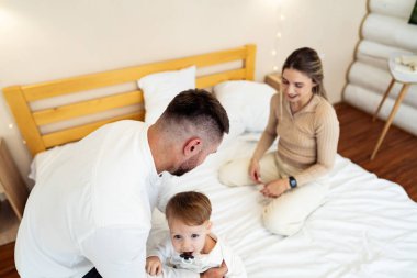 Bebek ile yatak odası eğlencesi. Ebeveynler, parlak, rahat bir yatak odasında, yürümeye başlayan çocuklarıyla neşe dolu anlar yaratıyorlar..