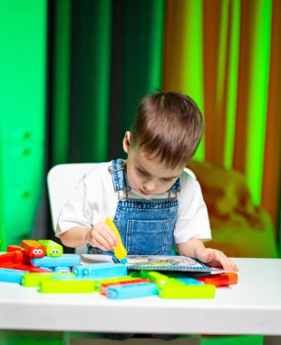 Çocuk oyuncaklarla boyamayı seviyor. Genç bir çocuk masasında parlak oyuncaklarla boyamaya odaklanır. Renkli bir ortamda eğlenceli bir aktiviteye katılır..