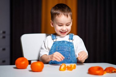 Mutlu çocuk evde portakallarla oynuyor. Genç bir çocuk kapalı bir ortamda masada otururken portakallarla oynamaktan ve soymaktan zevk alır..