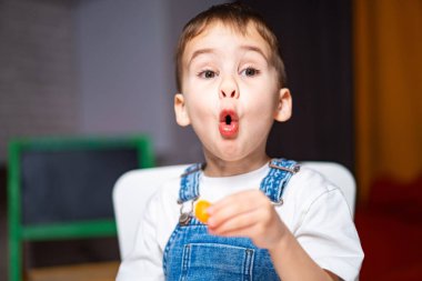 Genç çocuk evde lezzetli bir aperatifin tadını çıkarıyor. Tulum giymiş genç bir çocuk heyecanlı bir şekilde atıştırmalık bir şeyler tadıyor, ev ortamında neşe ve sürpriz gösteriyor..