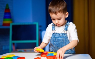Parlak yapı taşları olan bir çocuk. Genç bir çocuk, akşam saatlerinde bir masanın üzerine renkli yapı taşları dizmekle meşgul..