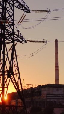 Elektrik hatları üzerinde güzel bir gün batımı. Gün batımında yüksek voltajlı güç kulesi manzarası. Dikey video