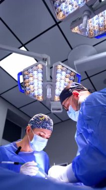 Kadın cerrah, erkek doktorun yardımıyla ameliyatta çalışıyor. Sıhhiye operasyonunda düşük açılı görüş. Dikey video.