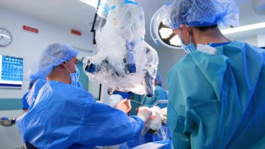 Mavi cüppeli doktor mikroskopta oturuyor ve asistanından bir enstrüman alıyor. Hastanede modern beyin cerrahisi.