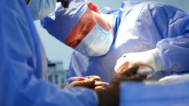 Maskeli tombul erkek doktor elinde bir aletle hastanın üzerine eğildi. Cerrahi hoparlörlerdeki tanınmamış cerrah eldivenli ellerde cihazlar tutuyor..