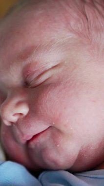 Yeni doğmuş bir bebeğin güzel, pembe yüzü huzur içinde uyuyor. Babamın eli bebeğin kulağını nazikçe okşar. Çocuk uyanıyor. Kapatın. Dikey video