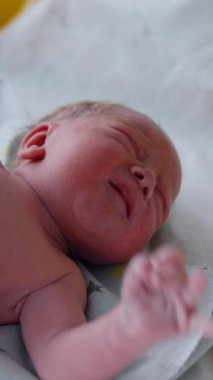 Yeni doğan doktor tarafından kontrol edilirken ağlıyor ve ellerini sallıyor. Doktor çocuğun uzunluğunu ölçmek için mezura kullanıyor. Kapatın. Dikey video