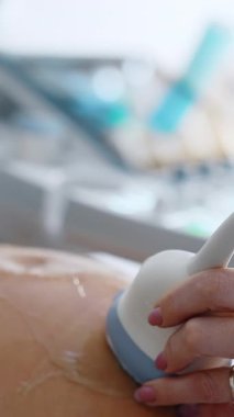 Doktor 'un eli, aleti büyük jöleli hamile karnına doğru hareket ettiriyor. Hamilelik gelişiminin ultrasonik incelemesi. Dikey video