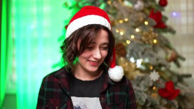Laptopta çalışan güzel, mutlu, beyaz bir bayan. Noel Baba şapkası takan esmer internetten iletişim kuruyor. Arkaplanda Noel ağacı.
