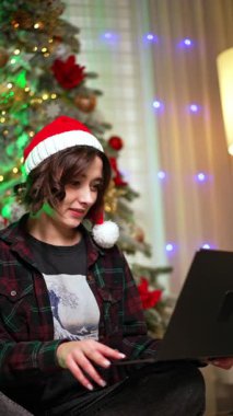 Noel Baba şapkalı kadın dizüstü bilgisayarına odaklanmış. Bayan Noel 'de evden çalışmak, alışveriş, iletişim ya da iş için bilgisayar kullanıyor. Dikey video.