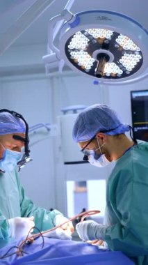 Cerrahi hoparlörlerdeki doktorlar ameliyat masasının iki tarafında dururlar. Erkek cerrahlar modern aletler ve aletler kullanır. Dikey video.