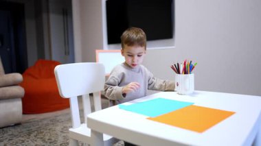 Masada resim yapan sevimli çocuk kalemini düşürdü. Sevimli çocuk eline kalem alıp çizmeye devam ediyor..