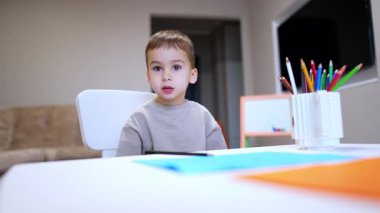 Tatlı erkek bebek masada oturup konuşuyor. Güzel çocuk bir kalem aldı ve çizmeye başladı. Düşük açı görünümü.