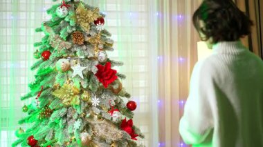 Süslü Noel ağacı kutlaması. Bir insan güzel süslenmiş Noel ağacına hayranlık duyar. Parlak süsler ve kapalı bir ortamda ışıklar..
